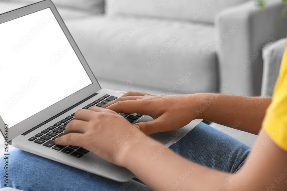 Young man using laptop on sofa at home, closeup Young man using laptop on sofa at home, closeup