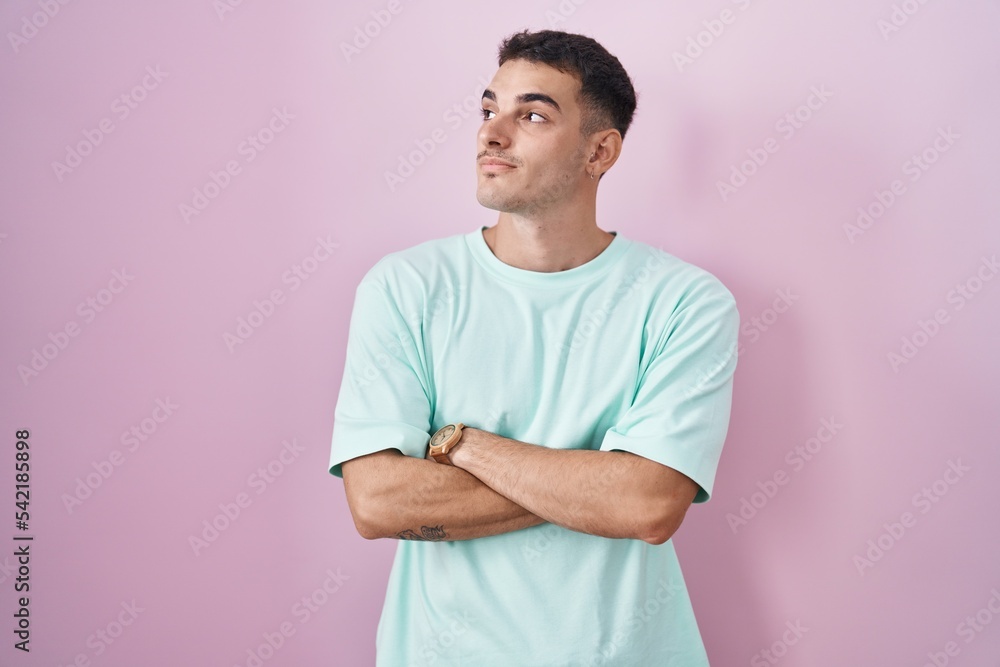 Handsome hispanic man standing over pink background looking to the side with arms crossed convinced and confident Handsome hispanic man standing over pink background looking to the side with arms crossed convinced and confident