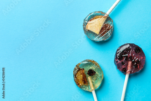 Sweet colorful lollipops with berries on light blue background, flat lay. Space for text