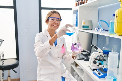 Young hispanic woman scientist pouring liquid on test tube at laboratory