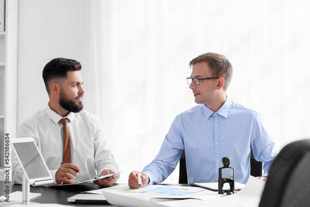 Male bank manager working with his colleague at table in office Male bank manager working with his colleague at table in office