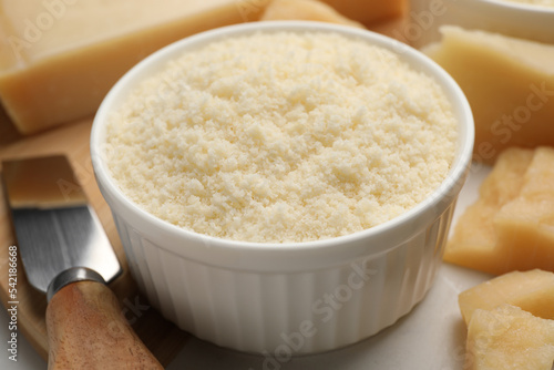Bowl with grated parmesan cheese on white table, closeup