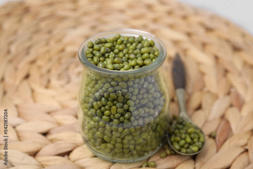 Glass jar of mung beans with spoon on wicker mat, closeup Glass jar of mung beans with spoon on wicker mat, closeup