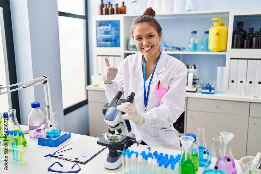 Young hispanic woman working at scientist laboratory smiling happy and positive, thumb up doing excellent and approval sign Young hispanic woman working at scientist laboratory smiling happy and positive, thumb up doing excellent and approval sign