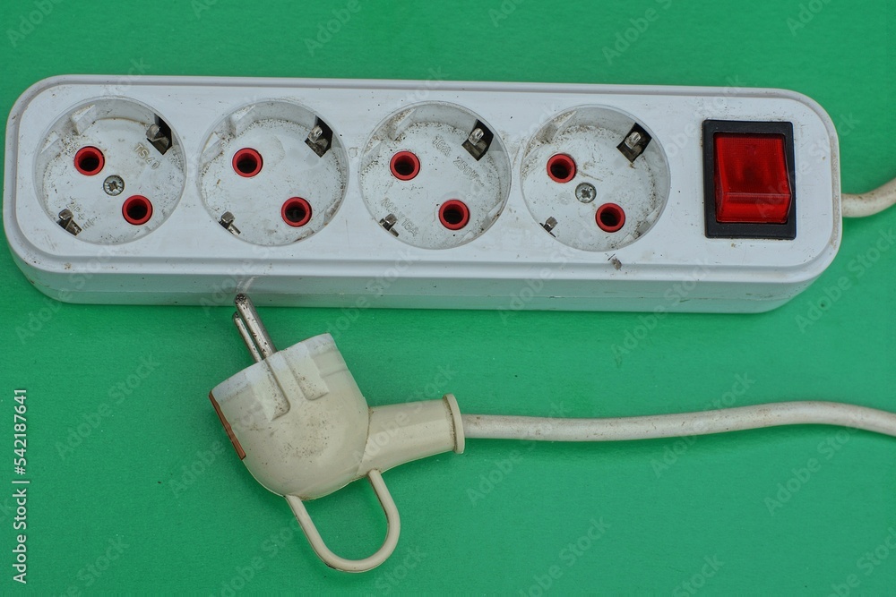 white old used plastic modern electric carrier with a powerful electric cable and plug lies on a green background white old used plastic modern electric carrier with a powerful electric cable and plug lies on a green background