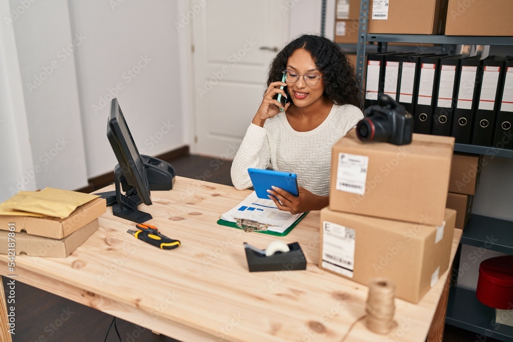 Young latin woman ecommerce business worker using touchpad talking on the smartphone at office Young latin woman ecommerce business worker using touchpad talking on the smartphone at office