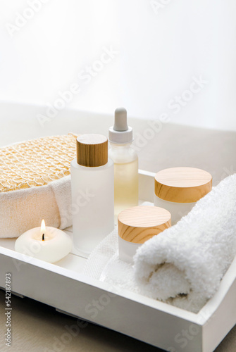 Various spa products on white tray, luxury spa relaxation concept. Massage oil, moisturizing creams, day cream, bath sponge, round candle burning, black lit.