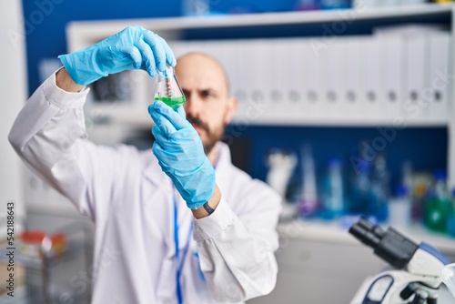 Young bald man scientist holding test tube at laboratory