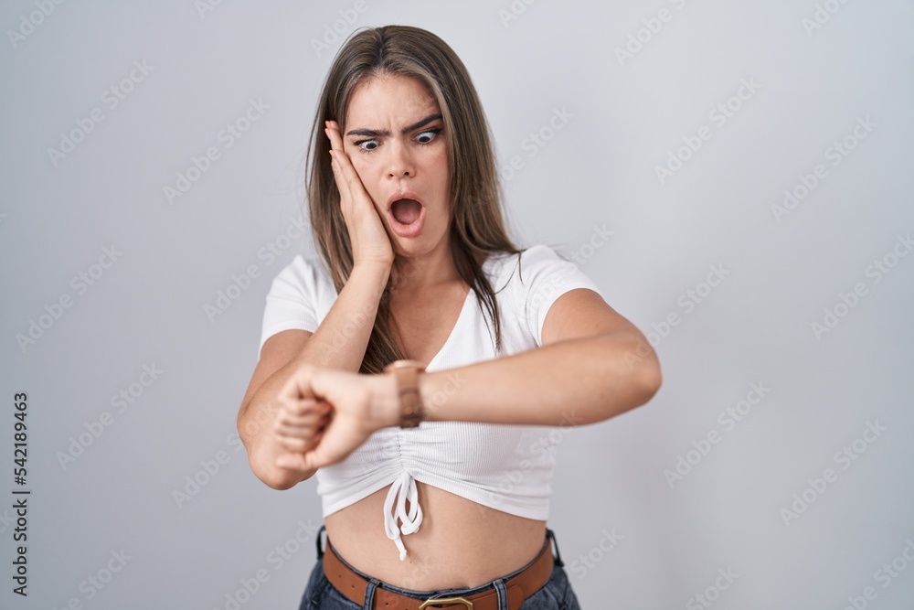Young beautiful woman wearing casual white t shirt looking at the watch time worried, afraid of getting late Young beautiful woman wearing casual white t shirt looking at the watch time worried, afraid of getting late