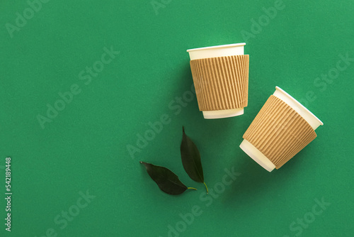 Paper cups and plant leaves on green background