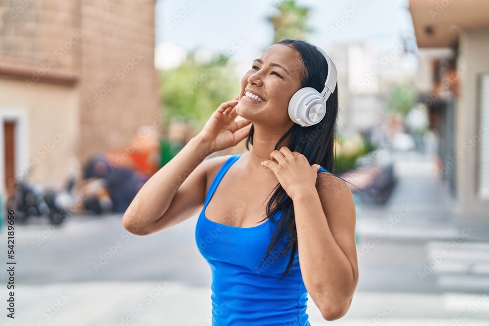 Young beautiful latin woman listening to music and dancing at street