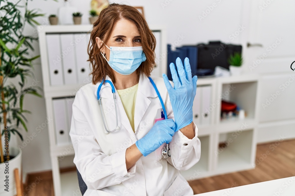 Middle age hispanic woman wearing doctor uniform and medical mask at clinic Middle age hispanic woman wearing doctor uniform and medical mask at clinic