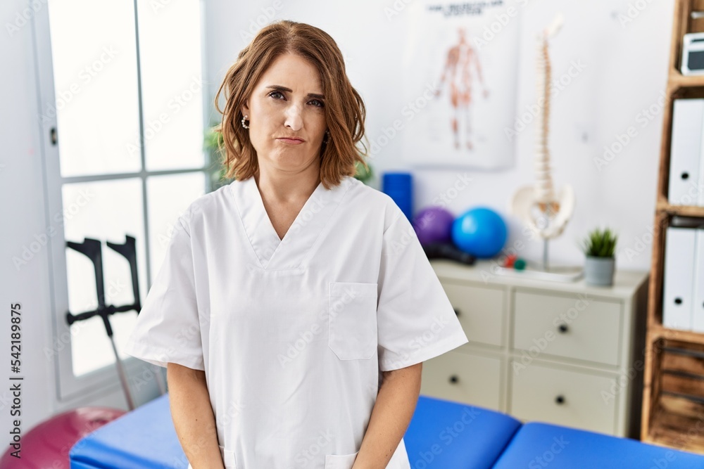 Middle age physiotherapist woman working at pain recovery clinic skeptic and nervous, frowning upset because of problem. negative person. Middle age physiotherapist woman working at pain recovery clinic skeptic and nervous, frowning upset because of problem. negative person.