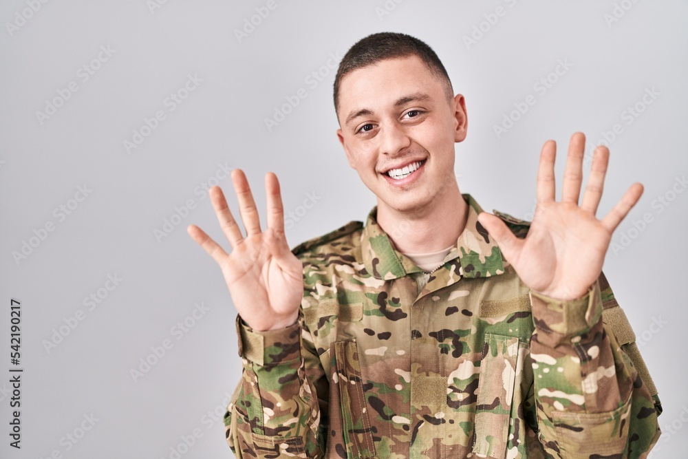 Young man wearing camouflage army uniform showing and pointing up with fingers number nine while smiling confident and happy. Young man wearing camouflage army uniform showing and pointing up with fingers number nine while smiling confident and happy.