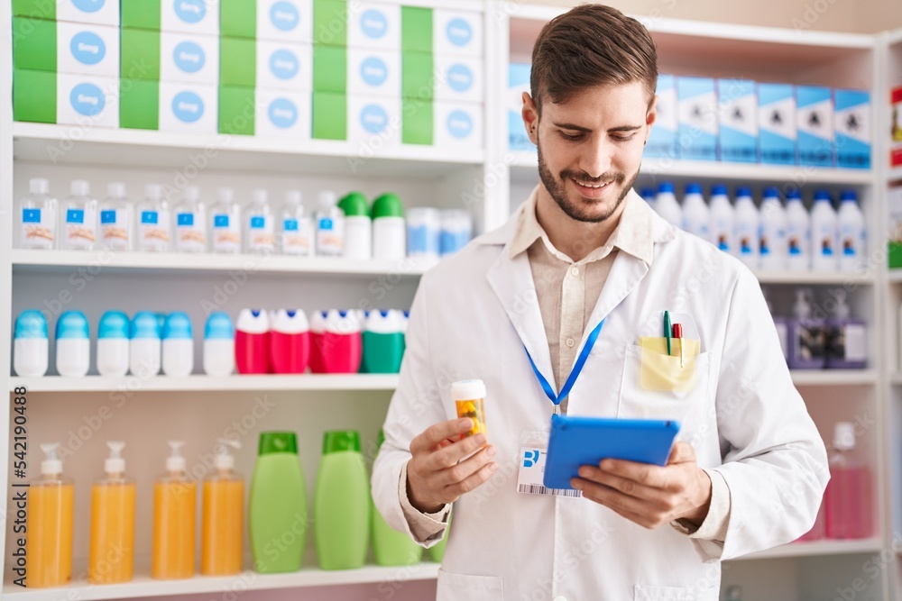 Young caucasian man pharmacist using touchpad holding pills at pharmacy