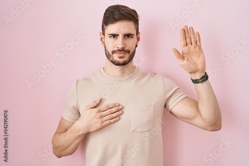 Hispanic man with beard standing over pink background swearing with hand on chest and open palm, making a loyalty promise oath © Krakenimages.com