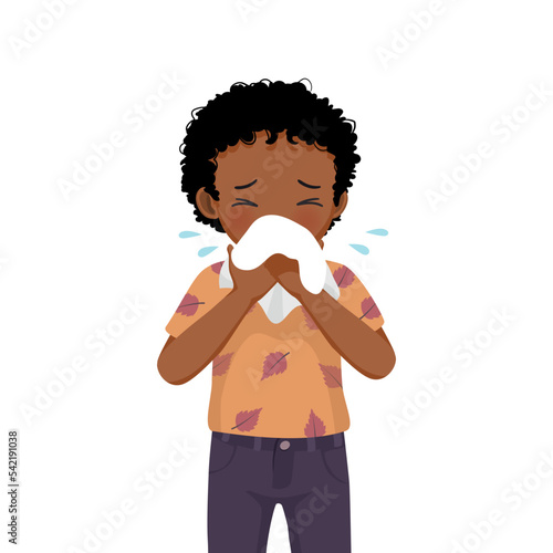 Cute little African boy sneezing with flu and cold allergic symptoms blowing nose into tissue paper 