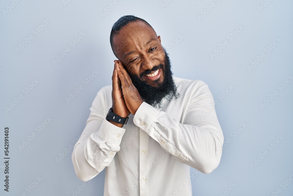 African american man standing over blue background sleeping tired dreaming and posing with hands together while smiling with closed eyes.