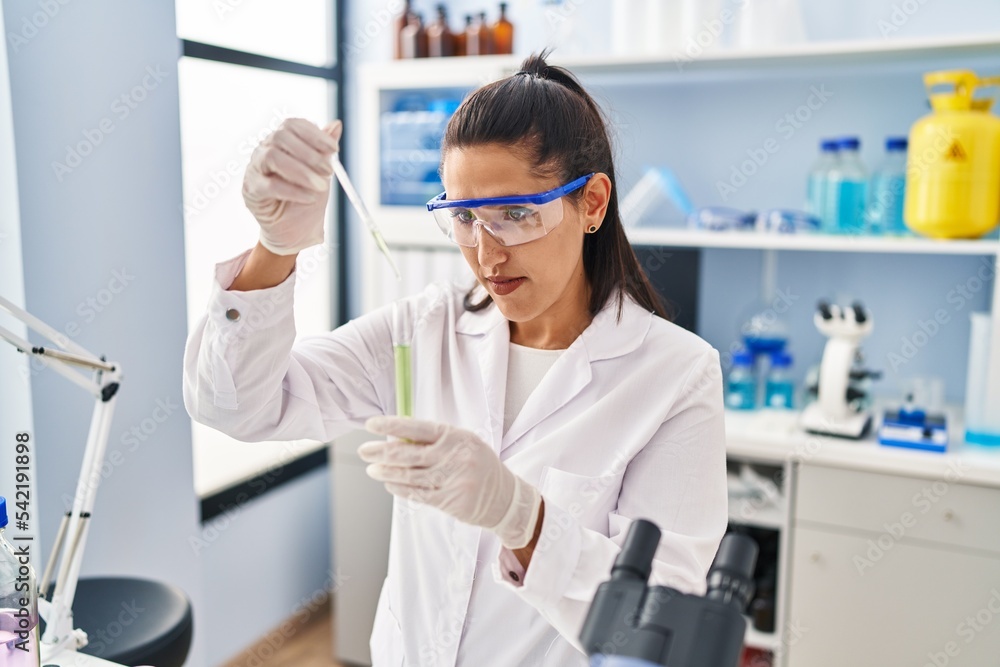 Young hispanic woman wearing scientist uniform using pipette working at laboratory Young hispanic woman wearing scientist uniform using pipette working at laboratory