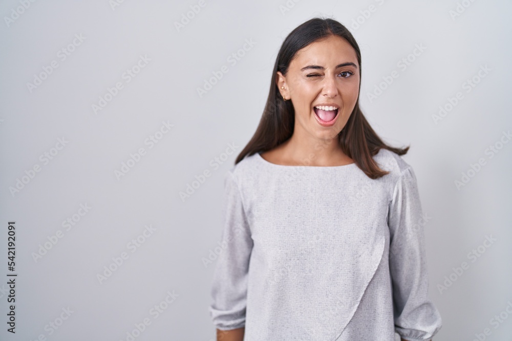 Young hispanic woman standing over white background winking looking at the camera with sexy expression, cheerful and happy face. Young hispanic woman standing over white background winking looking at the camera with sexy expression, cheerful and happy face.