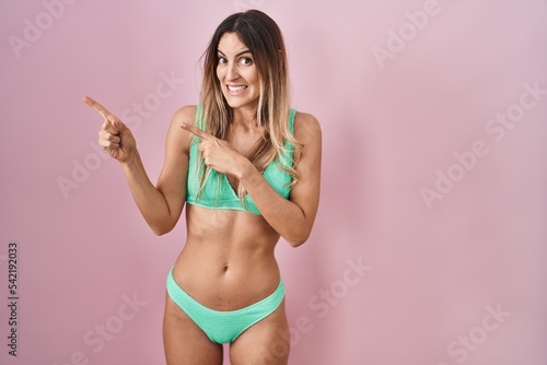 Young hispanic woman wearing bikini over pink background pointing aside worried and nervous with both hands, concerned and surprised expression