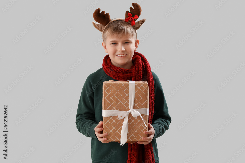 Happy little boy in reindeer horns with Christmas gift on light background Happy little boy in reindeer horns with Christmas gift on light background