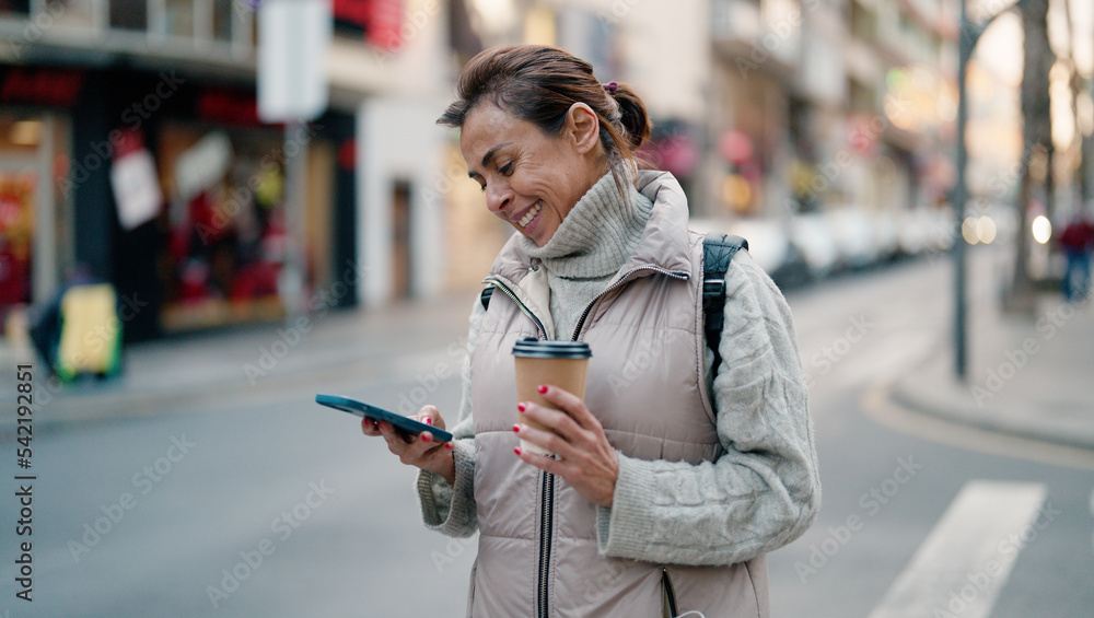 Obraz premium Middle age hispanic woman using smartphone drinking coffee at street