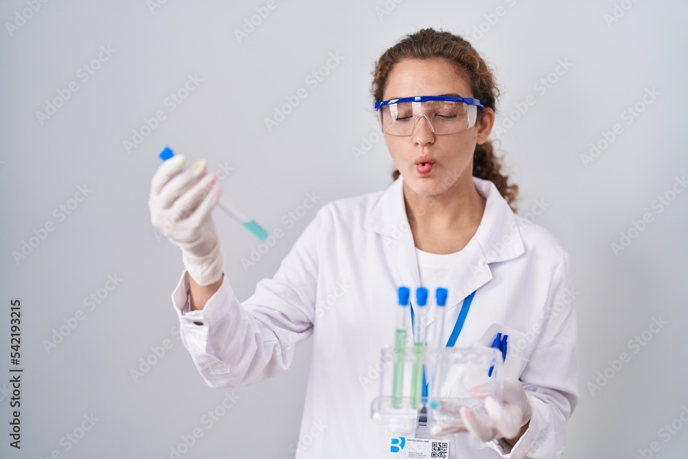 Young caucasian scientist woman working with laboratory samples making fish face with mouth and squinting eyes, crazy and comical. Young caucasian scientist woman working with laboratory samples making fish face with mouth and squinting eyes, crazy and comical.