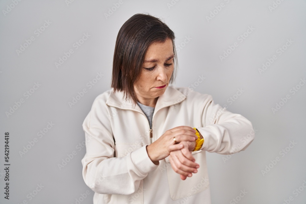 Middle age hispanic woman standing over isolated background checking the time on wrist watch, relaxed and confident Middle age hispanic woman standing over isolated background checking the time on wrist watch, relaxed and confident