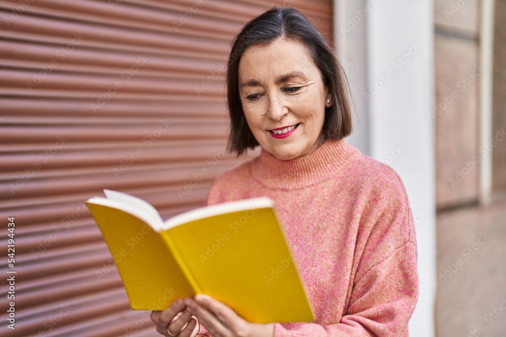 Middle age woman smiling confident reading book at street Middle age woman smiling confident reading book at street