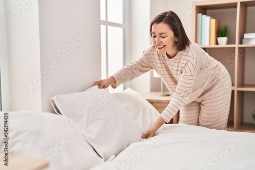 Middle age woman making bed standing at bedroom
