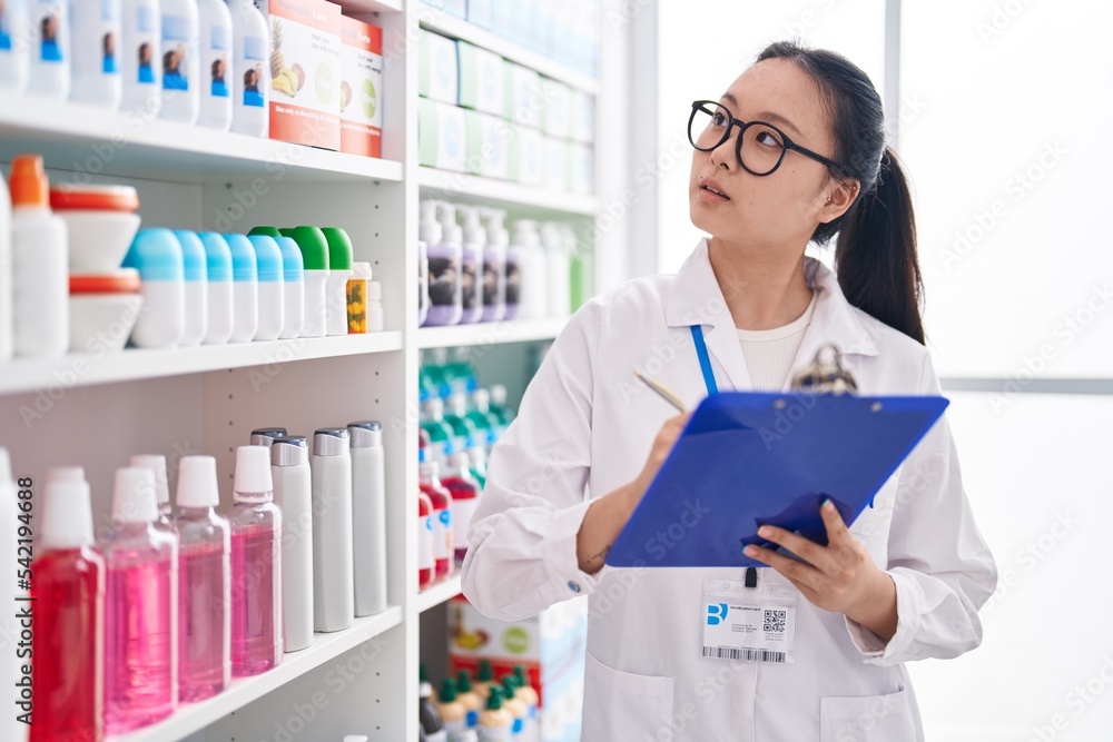 Young chinese woman pharmacist writing on document at pharmacy