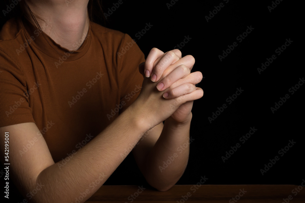 The girl folds her hands in prayer to God on a black background. prayer ...