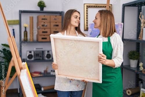Two women artists smiling confident holding draw canvas at art studio