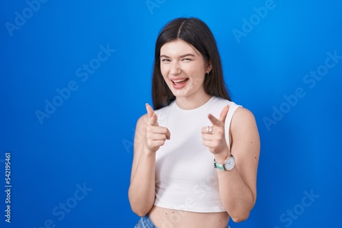 Young caucasian woman standing over blue background pointing fingers to camera with happy and funny face. good energy and vibes. © Krakenimages.com