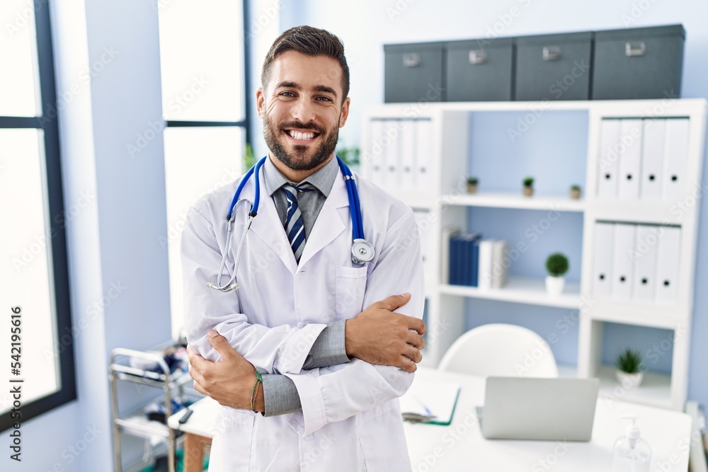 Handsome hispanic man wearing doctor uniform and stethoscope at medical clinic happy face smiling with crossed arms looking at the camera. positive person. Handsome hispanic man wearing doctor uniform and stethoscope at medical clinic happy face smiling with crossed arms looking at the camera. positive person.