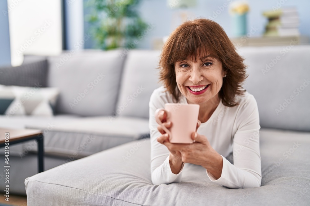Middle age woman drinking coffee lying on sofa at home