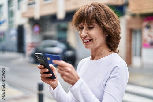 Middle age woman using smartphone and credit card at street