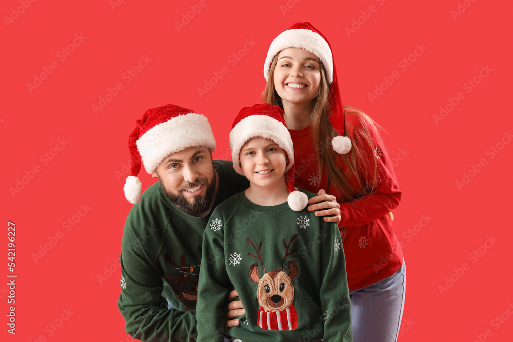 Happy parents with their little son in Santa hats on red background Happy parents with their little son in Santa hats on red background