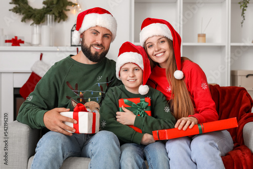 Happy parents with their little son in Santa hats with presents at home on Christmas eve