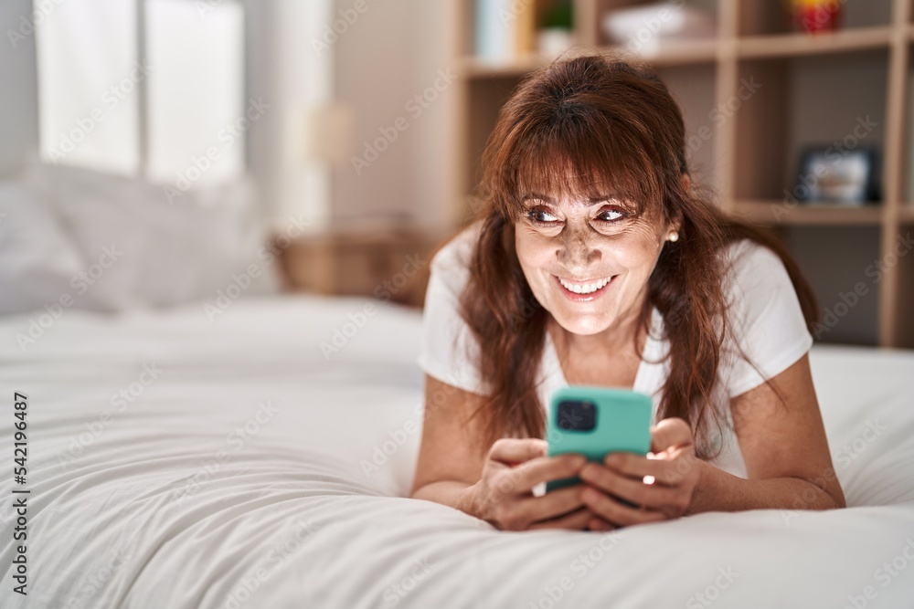 Middle age woman using smartphone lying on bed at bedroom Middle age woman using smartphone lying on bed at bedroom