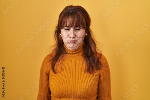 Middle age hispanic woman standing over yellow background puffing cheeks with funny face. mouth inflated with air, crazy expression. © Krakenimages.com