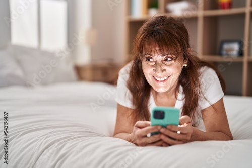 Middle age woman using smartphone lying on bed at bedroom