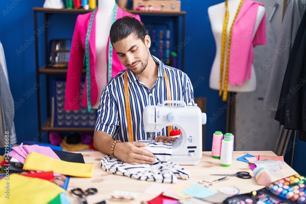Fototapeta premium Young hispanic man tailor smiling confident using sewing machine at sewing studio