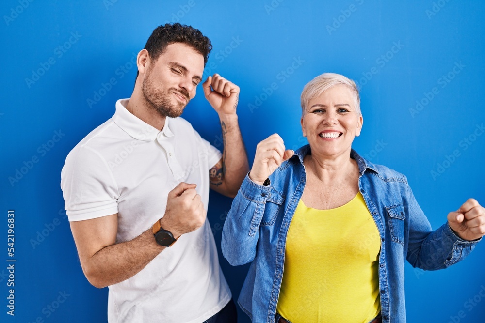 Young brazilian mother and son standing over blue background dancing happy and cheerful, smiling moving casual and confident listening to music Young brazilian mother and son standing over blue background dancing happy and cheerful, smiling moving casual and confident listening to music