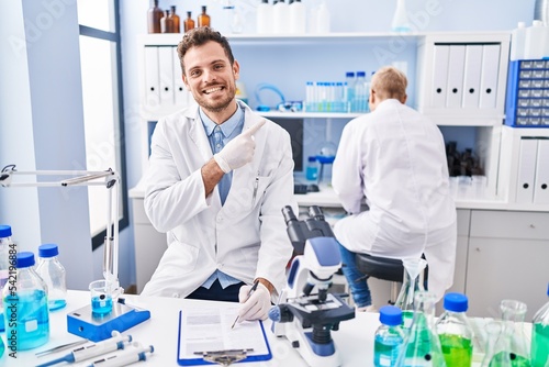 Hispanic man and woman working at scientist laboratory smiling happy pointing with hand and finger to the side
