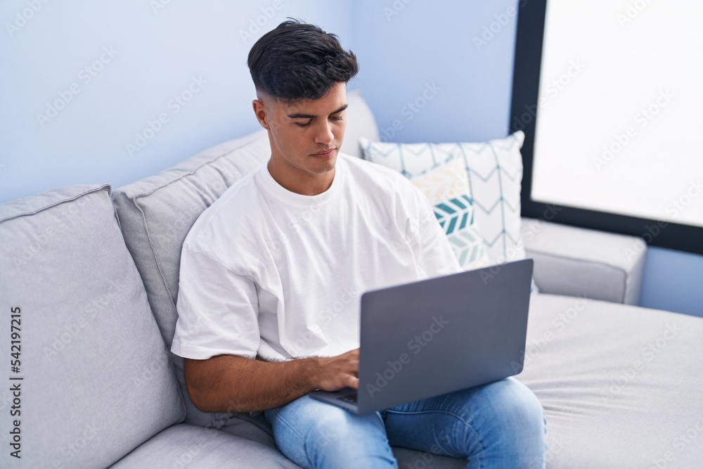 Young hispanic man using laptop sitting on table at home Young hispanic man using laptop sitting on table at home