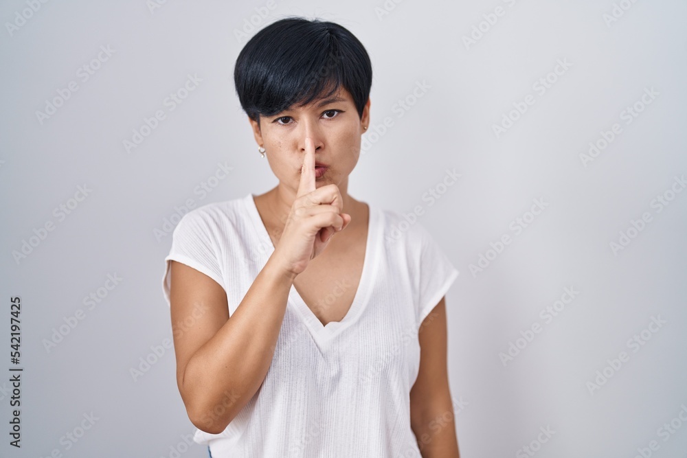 Young asian woman with short hair standing over isolated background asking to be quiet with finger on lips. silence and secret concept. Young asian woman with short hair standing over isolated background asking to be quiet with finger on lips. silence and secret concept.