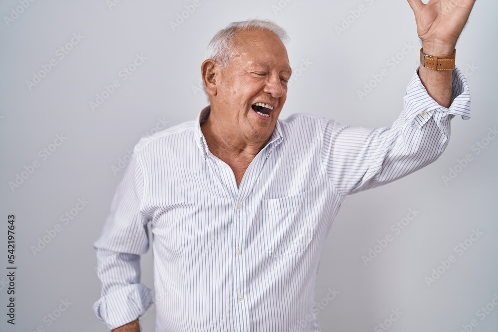 Senior man with grey hair standing over isolated background dancing happy and cheerful, smiling moving casual and confident listening to music Senior man with grey hair standing over isolated background dancing happy and cheerful, smiling moving casual and confident listening to music