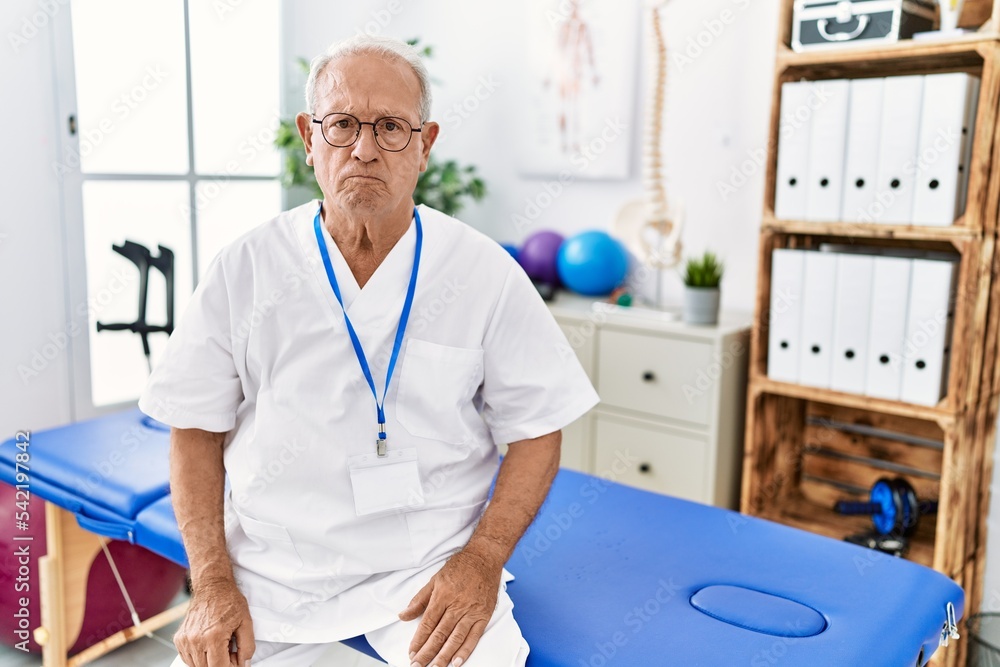Fototapeta premium Senior physiotherapy man working at pain recovery clinic skeptic and nervous, frowning upset because of problem. negative person.